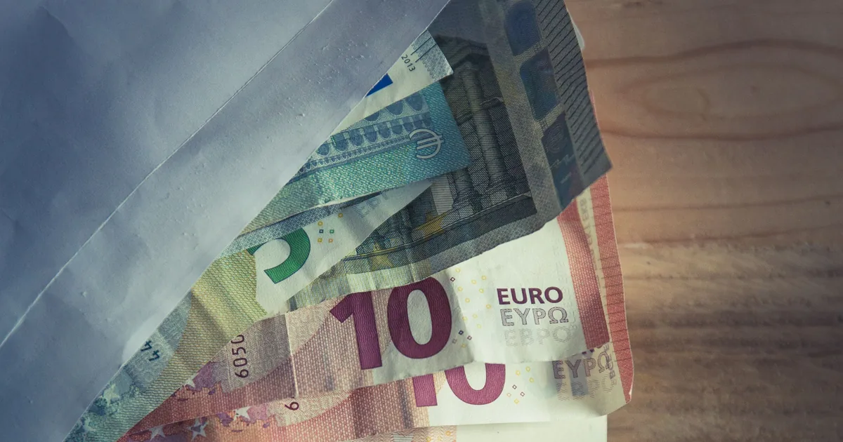 Un sobre con billetes de euro sobre una mesa de madera, los billetes asoman en abanico del sobre